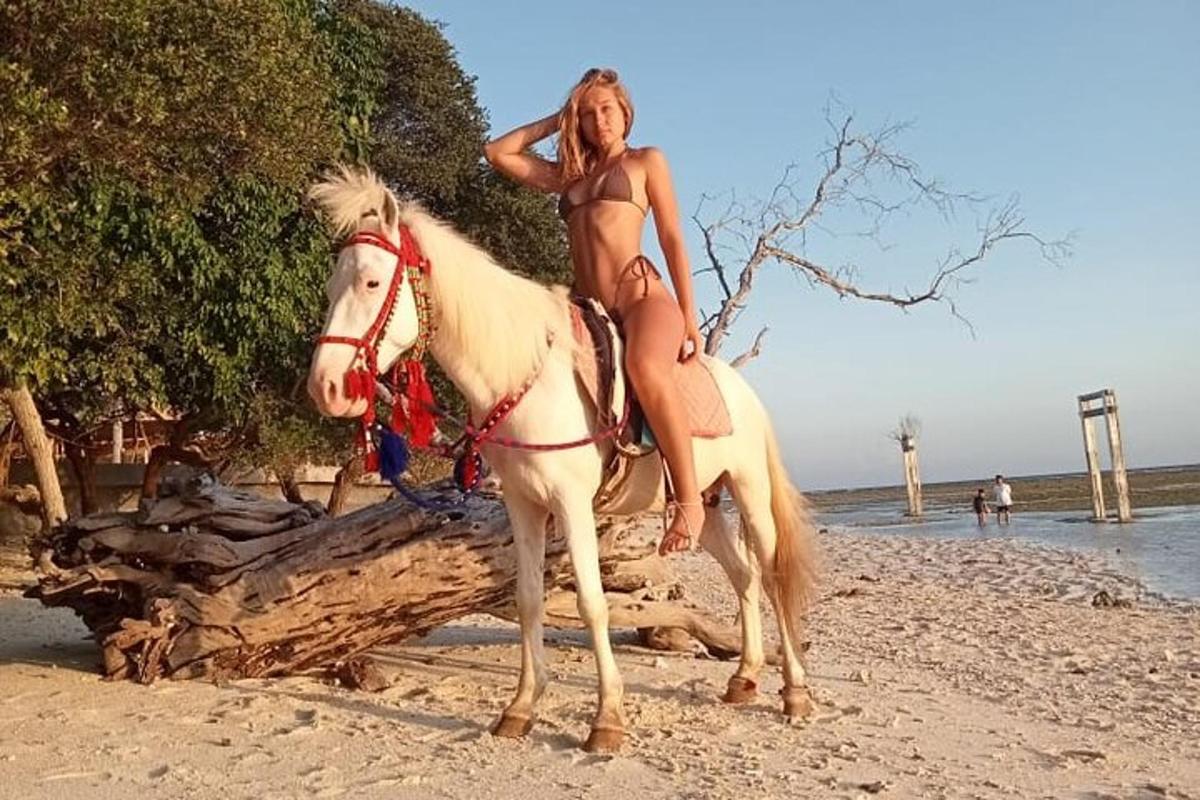 a woman in a bikini riding a horse on the beach