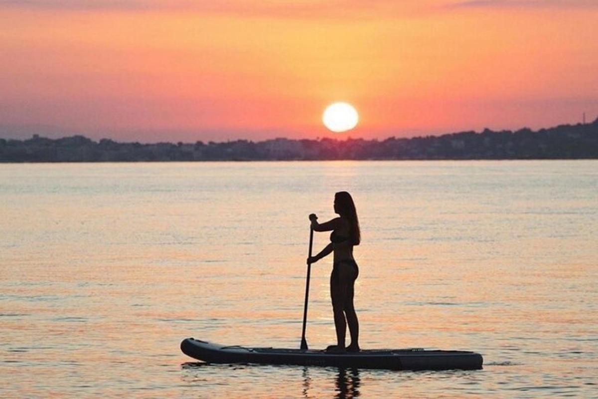 žena stojící na paddleboardu ve vodě při západu slunce