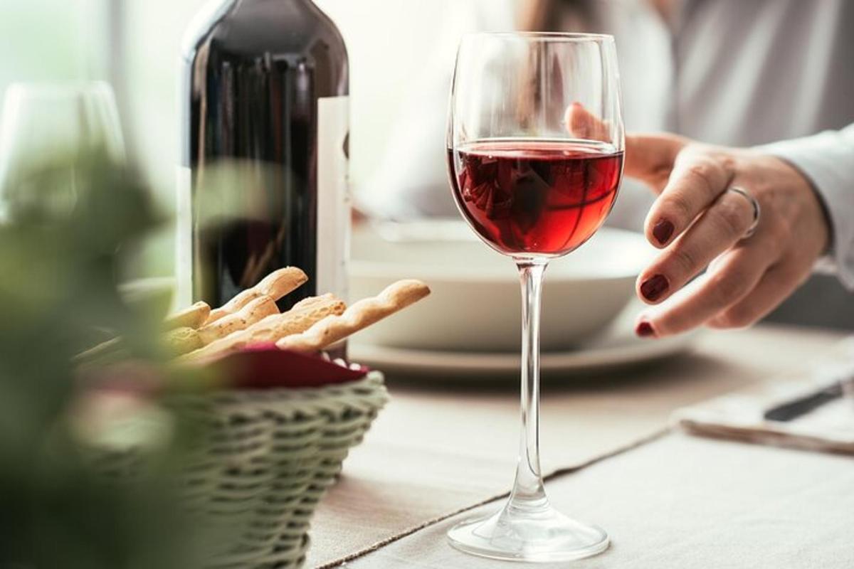 uma pessoa segurando uma taça de vinho ao lado de uma cesta de comida
