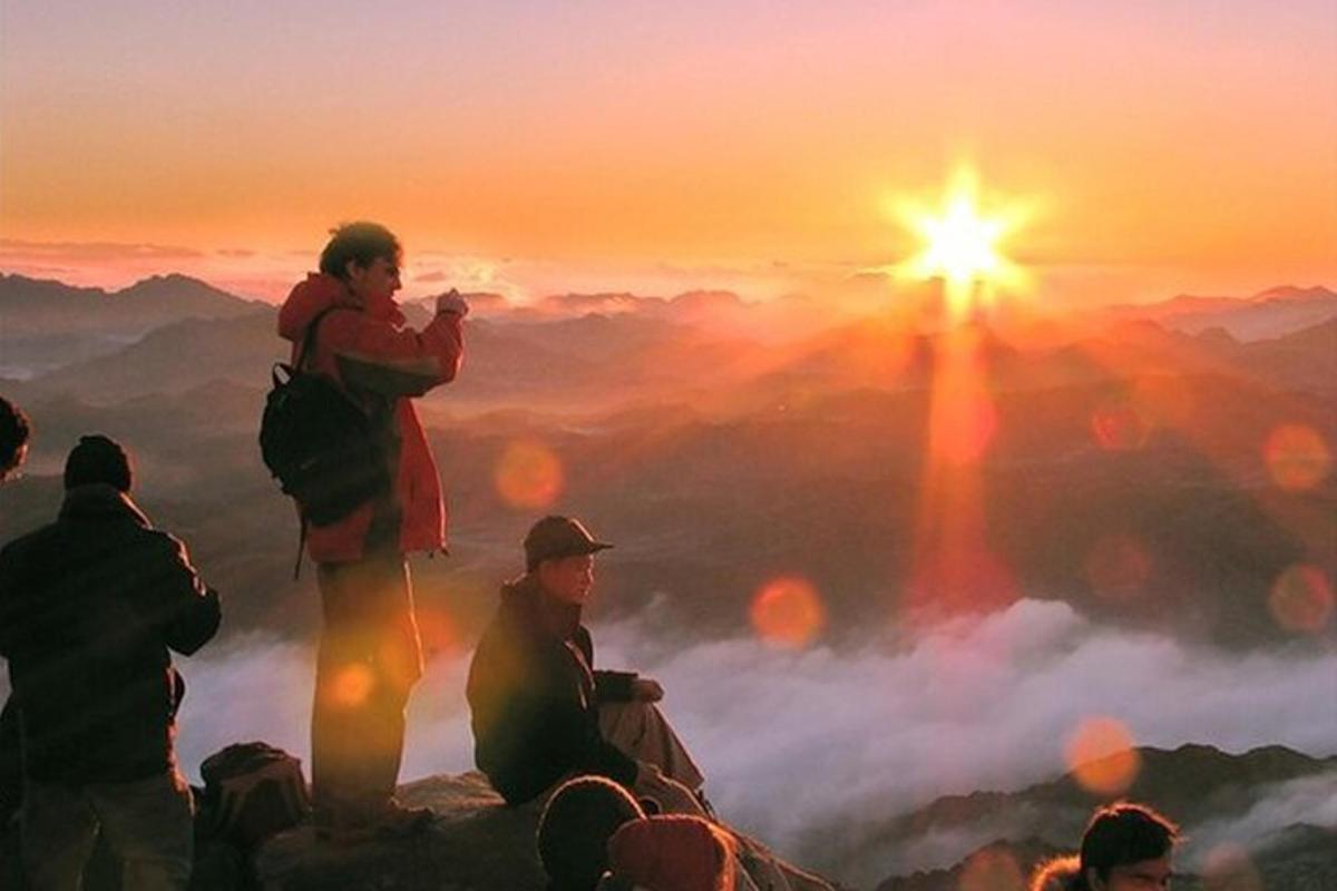 en gruppe mennesker som står på toppen av et fjell ved solnedgang