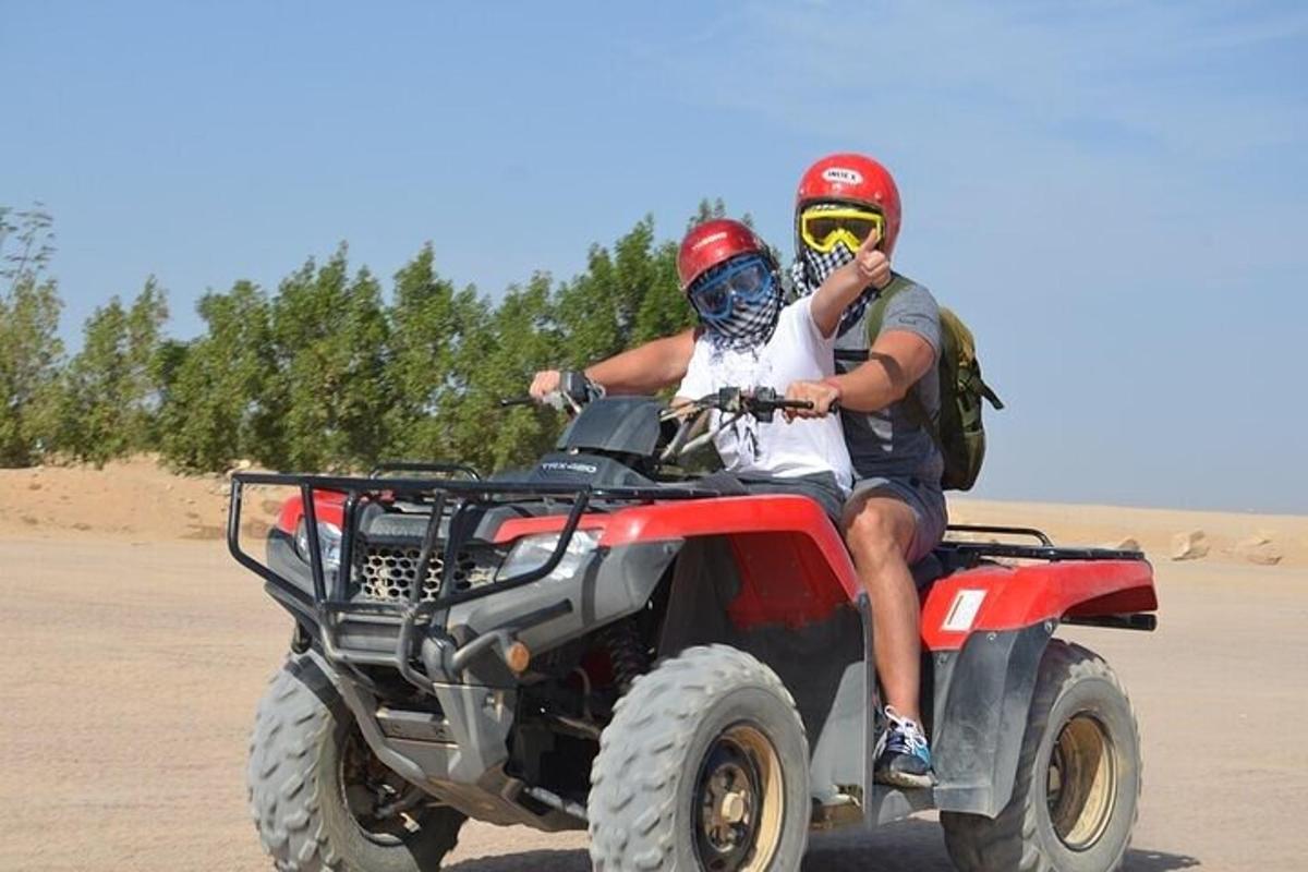 zwei Personen fahren auf einem Quad in der Wüste