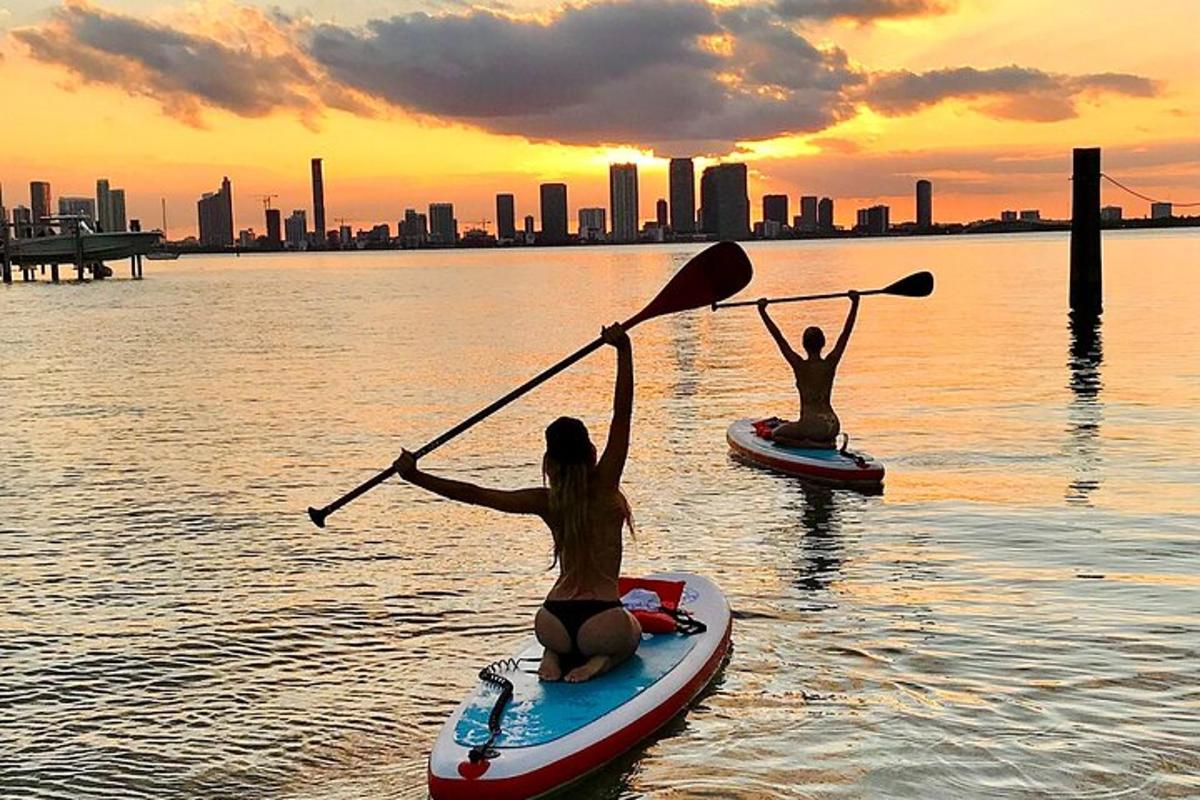 dues persones sobre taules de paddle surf a l'aigua amb la ciutat