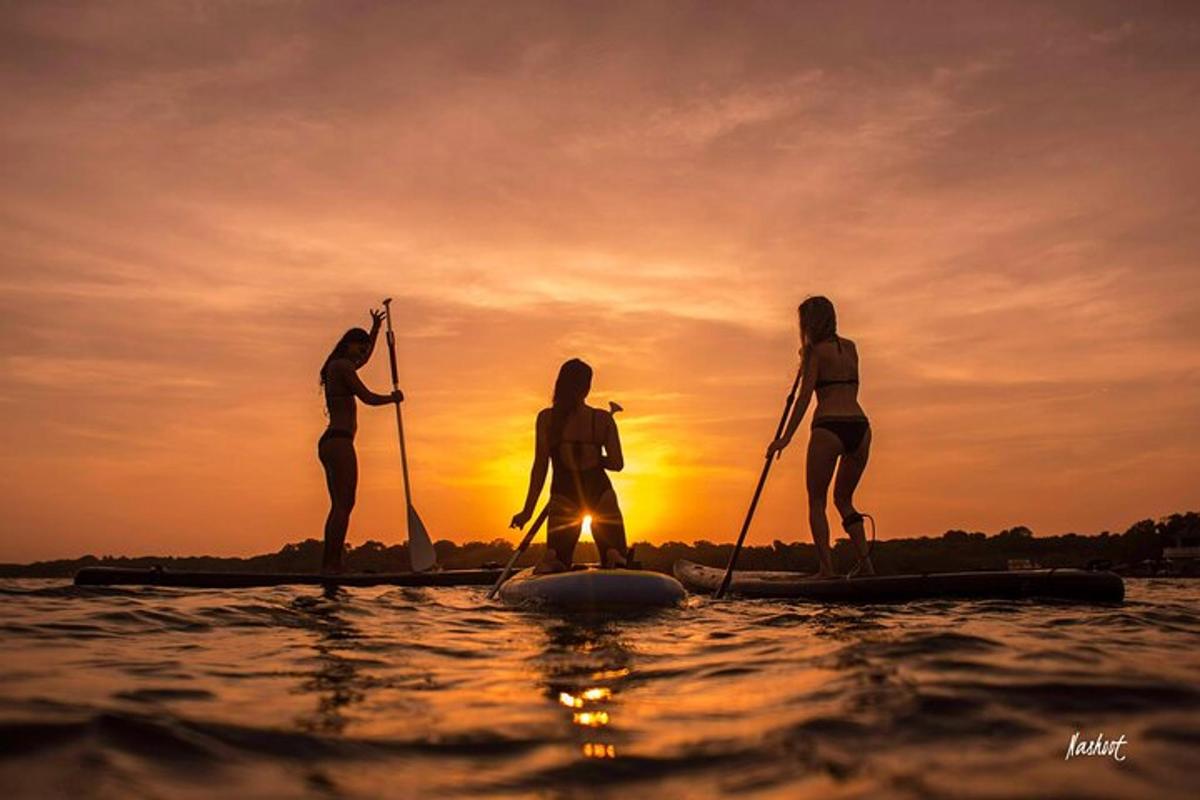 tre persone su una tavola da paddle in acqua al tramonto