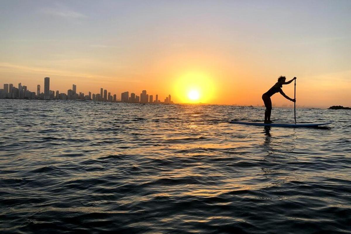 seseorang di atas papan dayung di dalam air pada waktu matahari terbenam