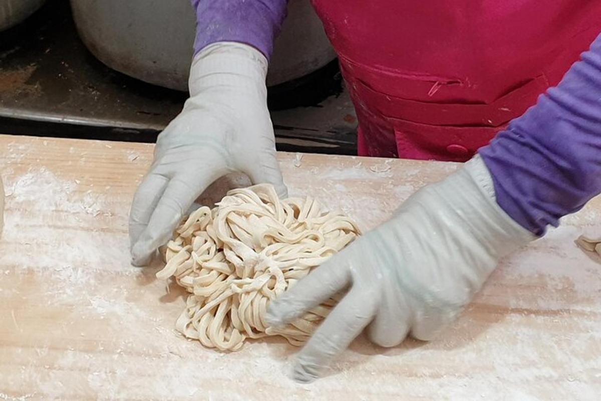 una persona amb guants fent fideus en una taula de tallar