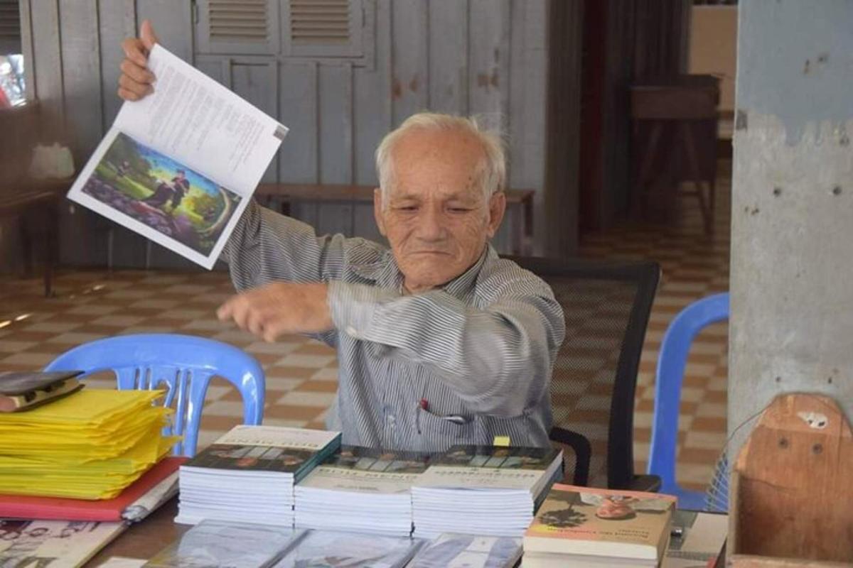 Un hombre mayor sentado en una mesa sosteniendo un periódico