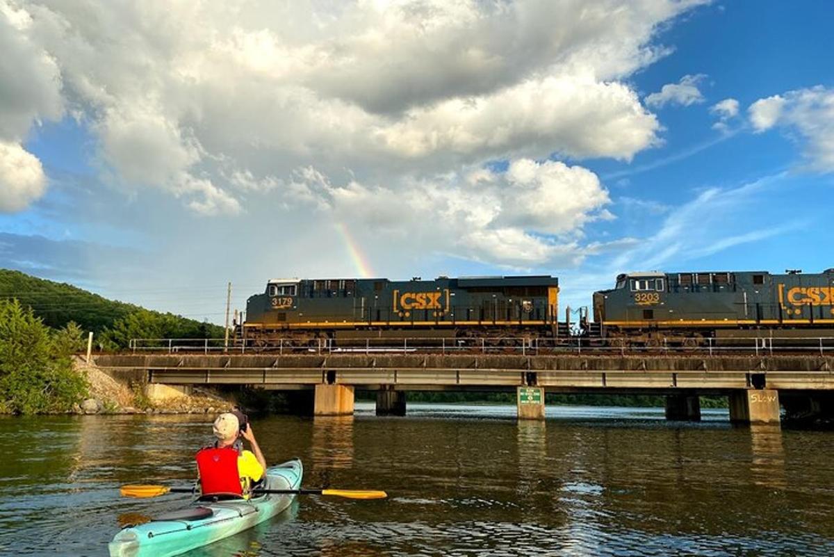 a man in a kayak on a river with a train