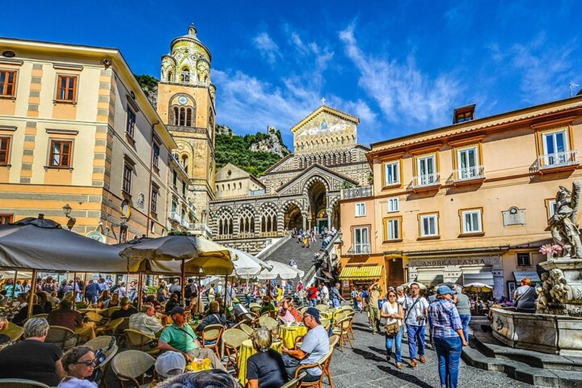 tłum ludzi siedzących przy stołach na ulicy z wieżą zegarową