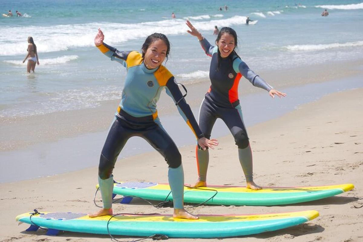 dues noies estan dretes sobre taules de surf a la platja
