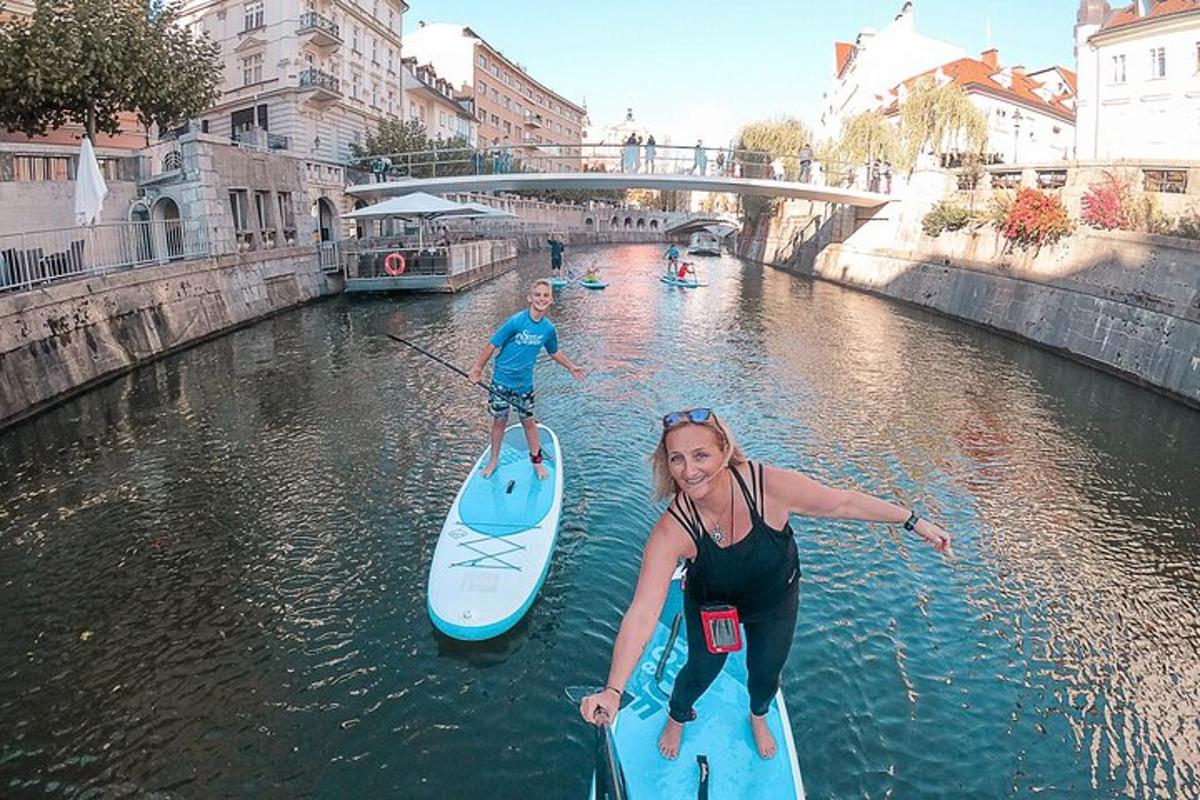 Două persoane stau pe plăci de paddle într-un râu