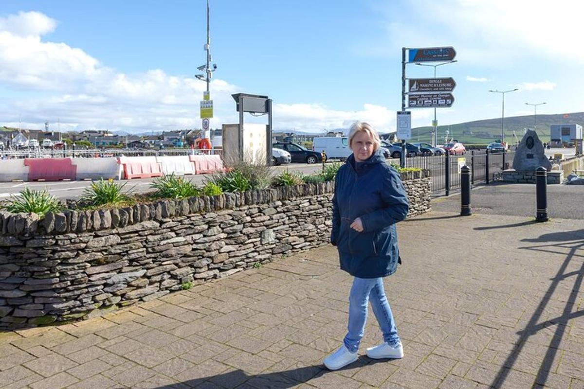 kona stendur á gangstétt við hliðina á steinvegg