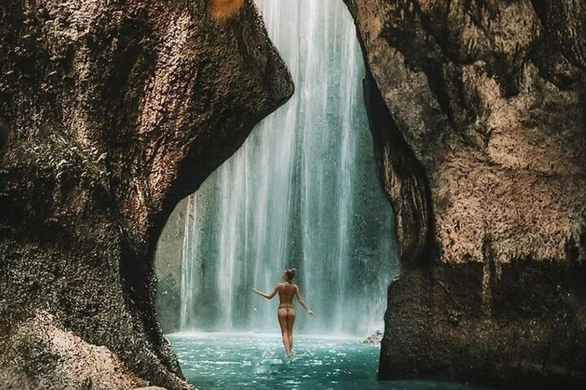 seorang wanita berjalan di dalam air di hadapan air terjun