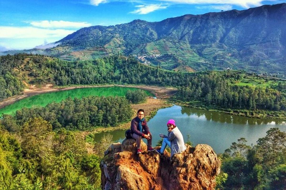 dua orang duduk di atas batu yang menghadap ke tasik