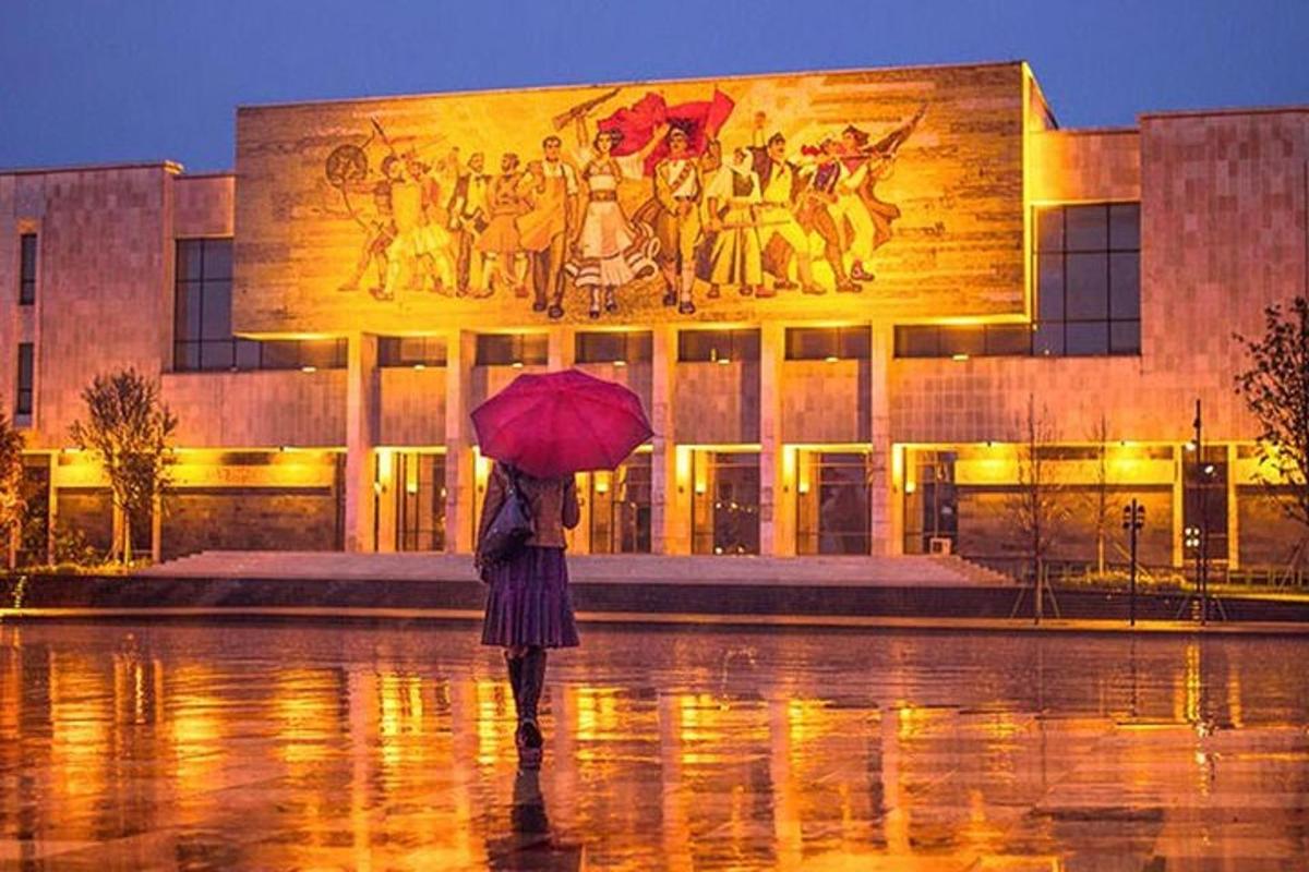 una dona caminant sota la pluja amb un paraigua davant d'un edifici