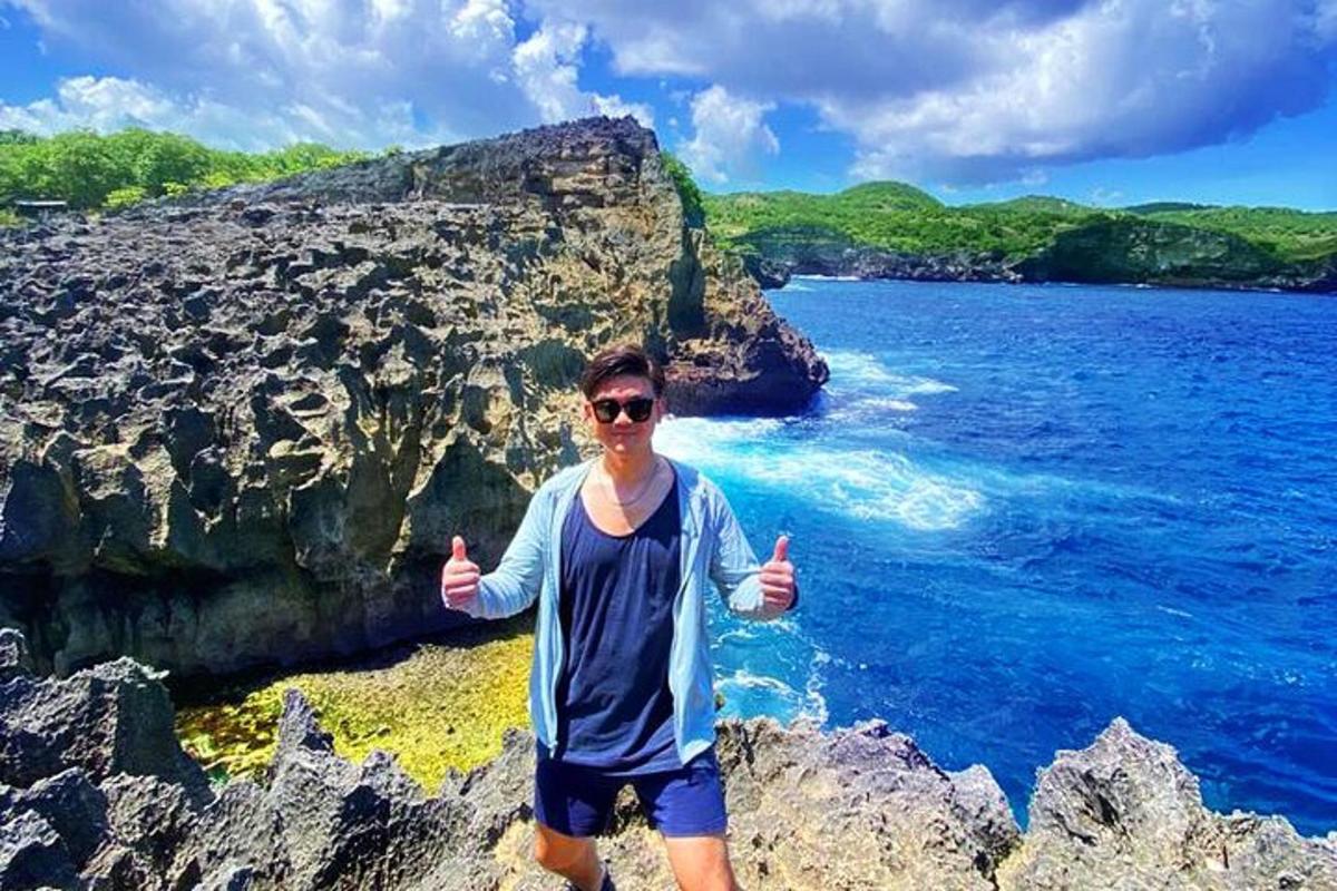 un uomo che fa il gesto del pollice in su mentre è in piedi su una spiaggia rocciosa