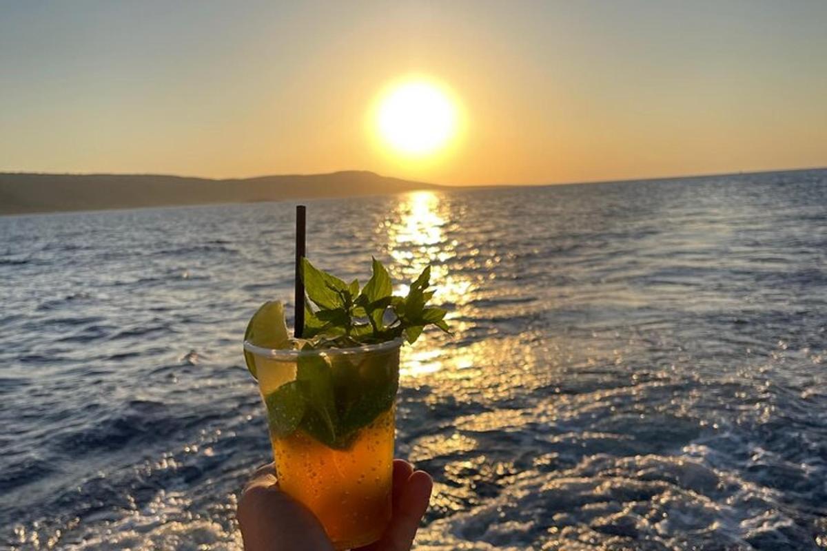 a person holding a drink with the sunset in the background