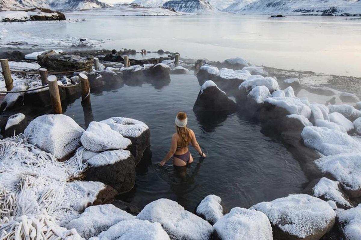 una donna in piedi in uno specchio d'acqua con rocce coperte di neve