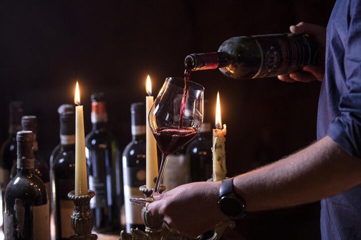 a person pouring wine into a wine glass with candles