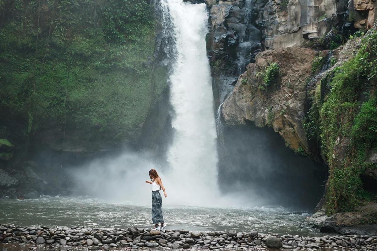 Una mujer parada sobre rocas frente a una cascada.