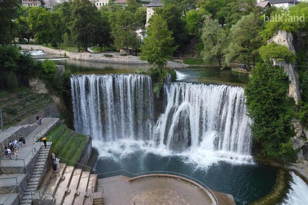 Una cascada en un parque con gente parada frente a ella.