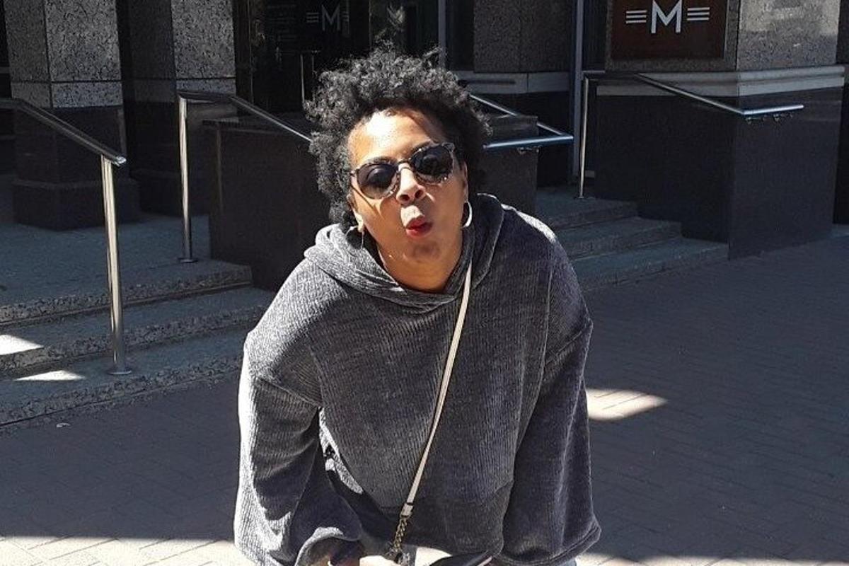 Una mujer con gafas de sol sentada en la acera con la boca abierta.