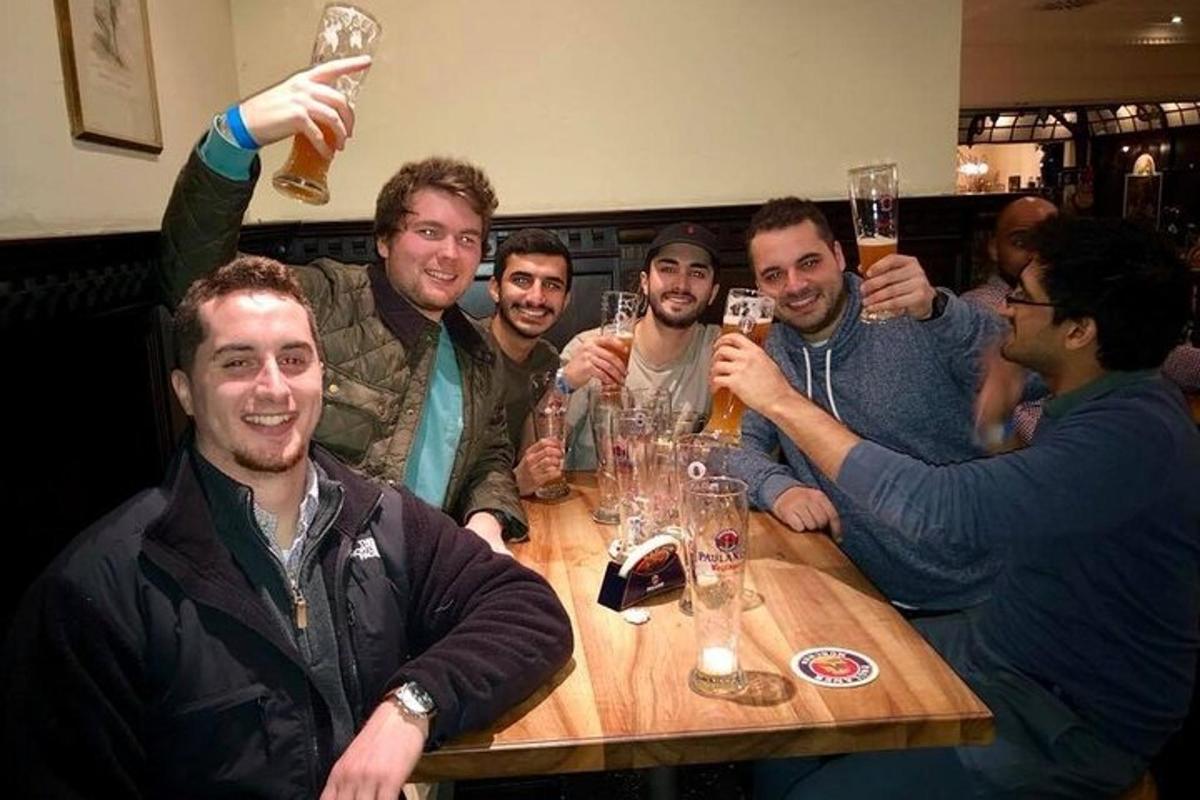 een groep mannen die rond een tafel zitten en bier drinken