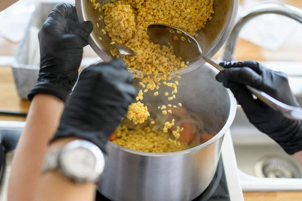 une personne portant des gants noirs cuisinant des aliments dans une casserole