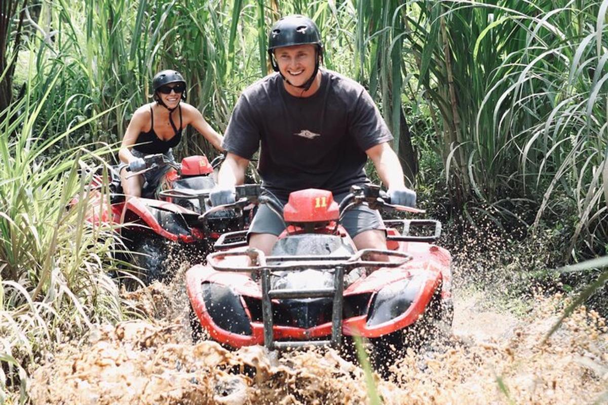 two people riding on four wheelers through the mud