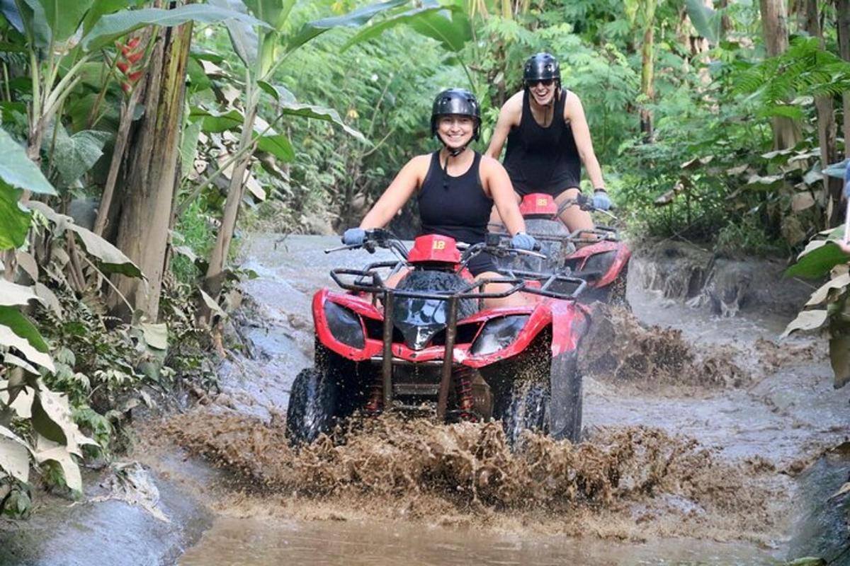 two people riding on a four wheeler through a muddy trail