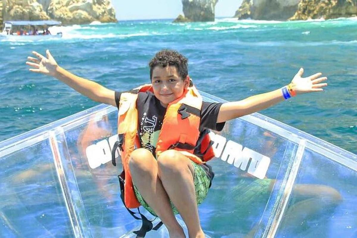 a young boy sitting on a glass boat in the water