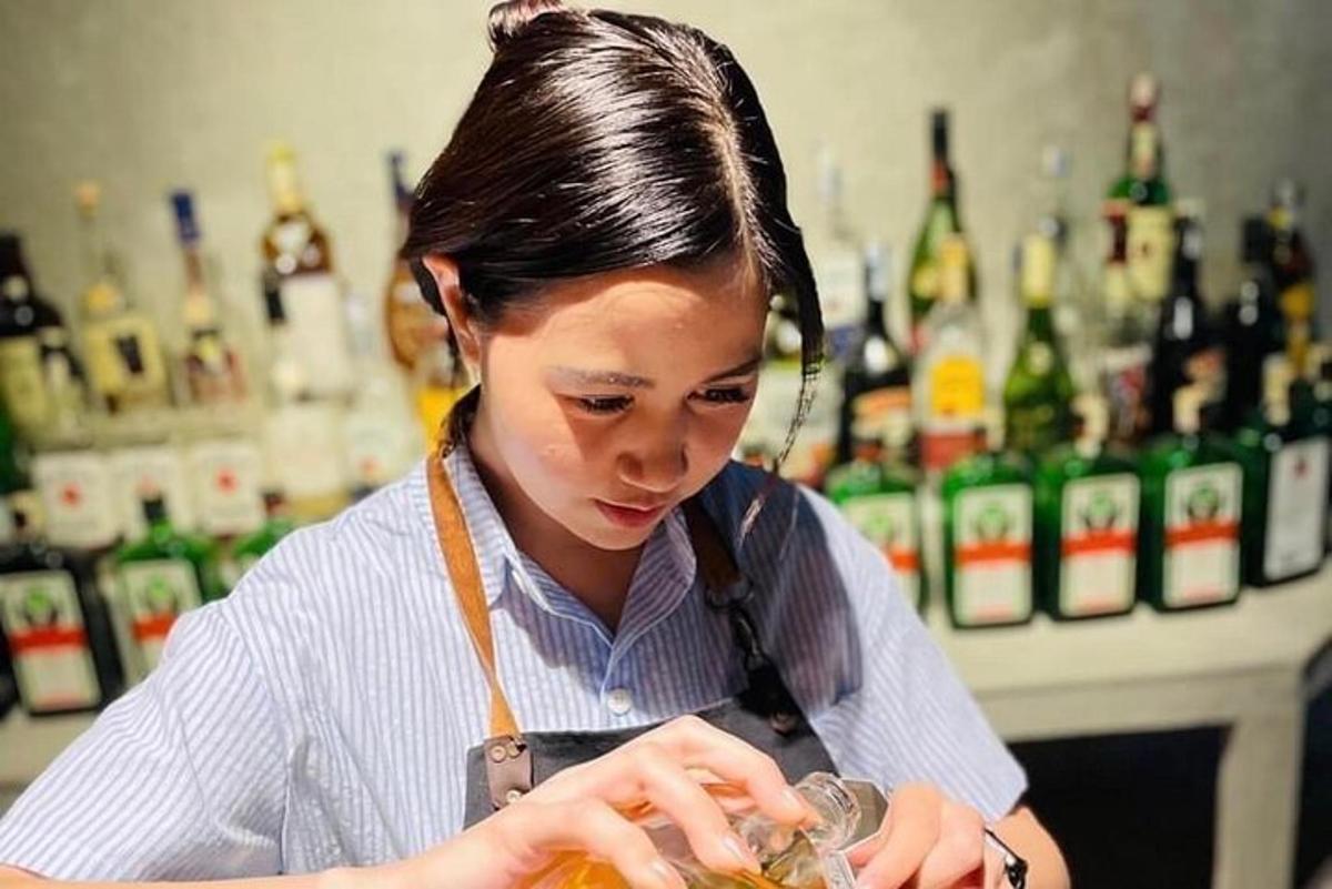 a woman standing at a bar mixing a drink