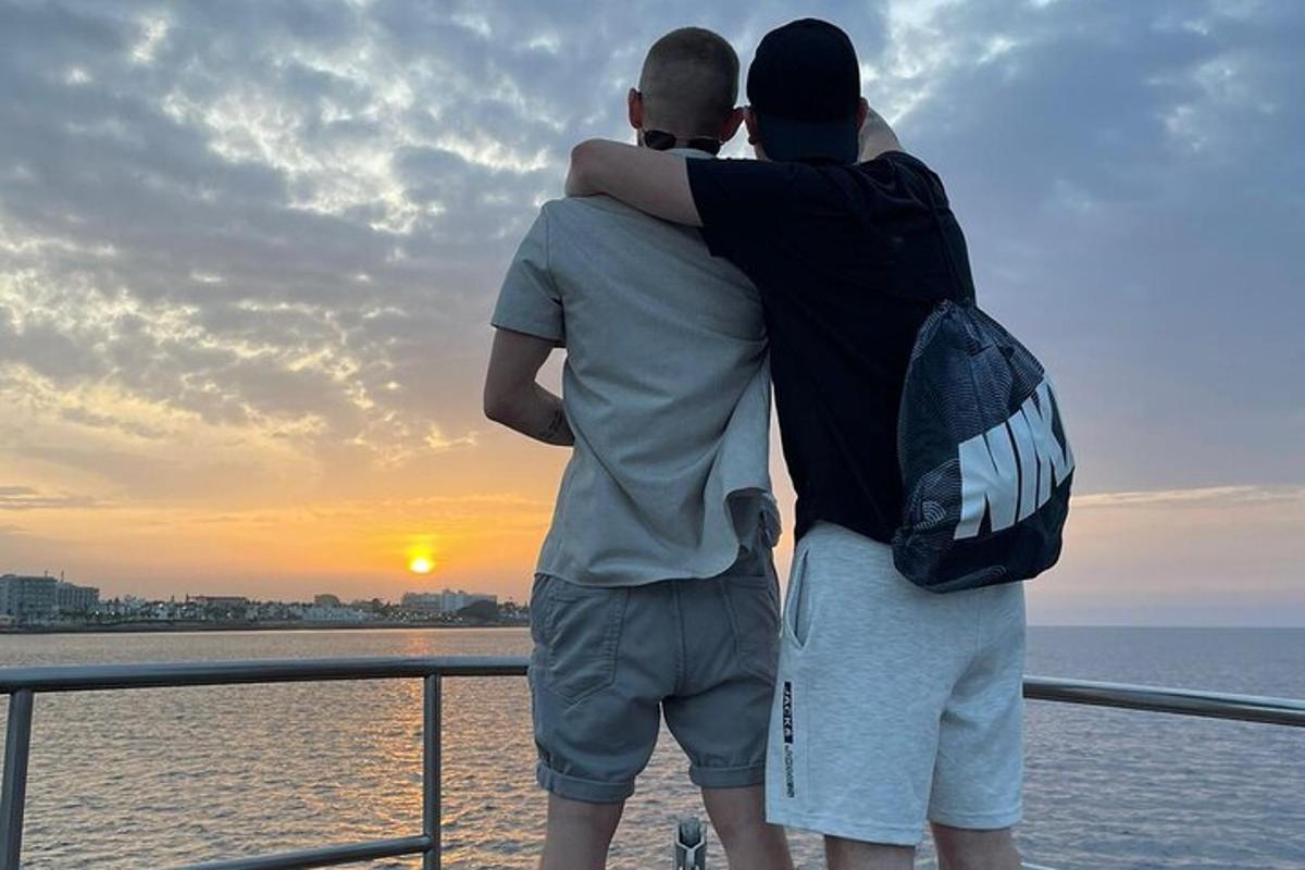dva muži stojící na trajektu a sledující západ slunce