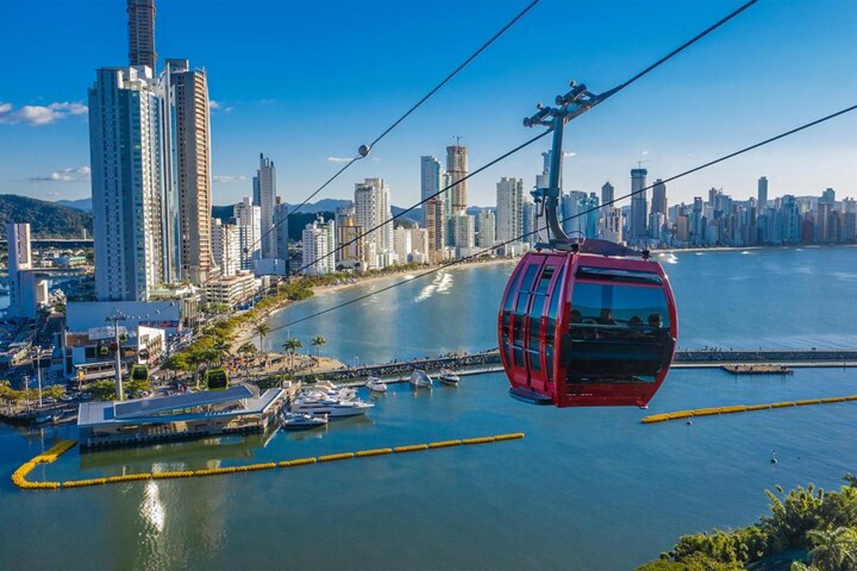 a red cable car flying over a river with a city
