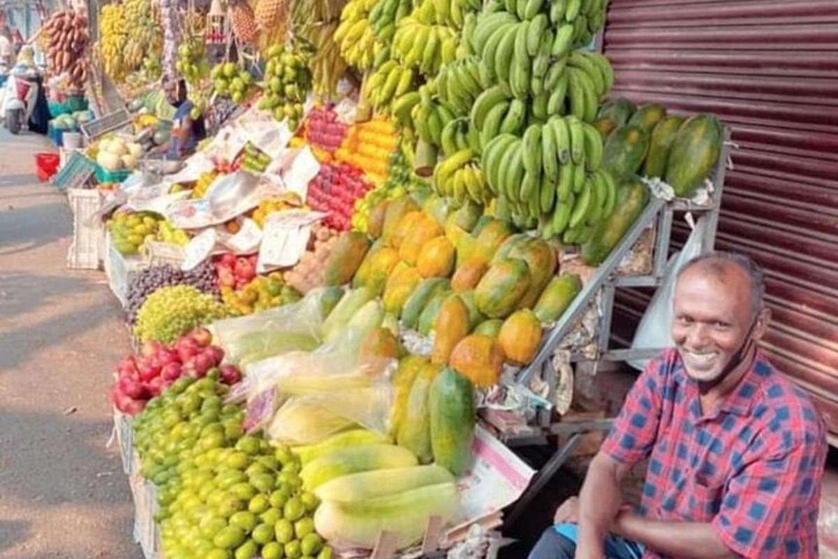 un bărbat așezat în fața unei tarabe cu fructe