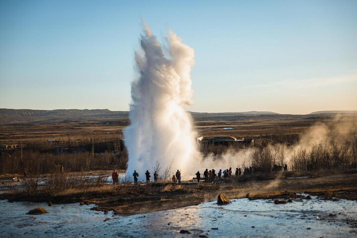 en stor geysir med utbrudd og folk som står rundt den
