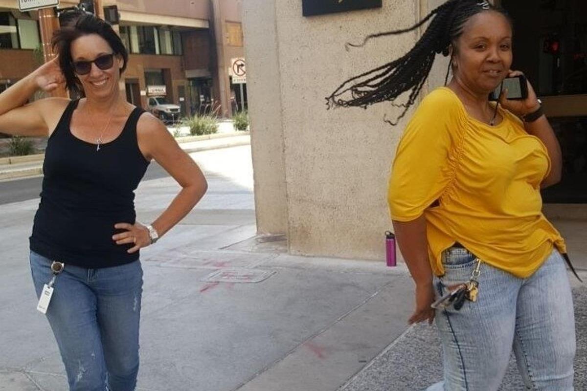 two women standing on a sidewalk talking on a cell phone