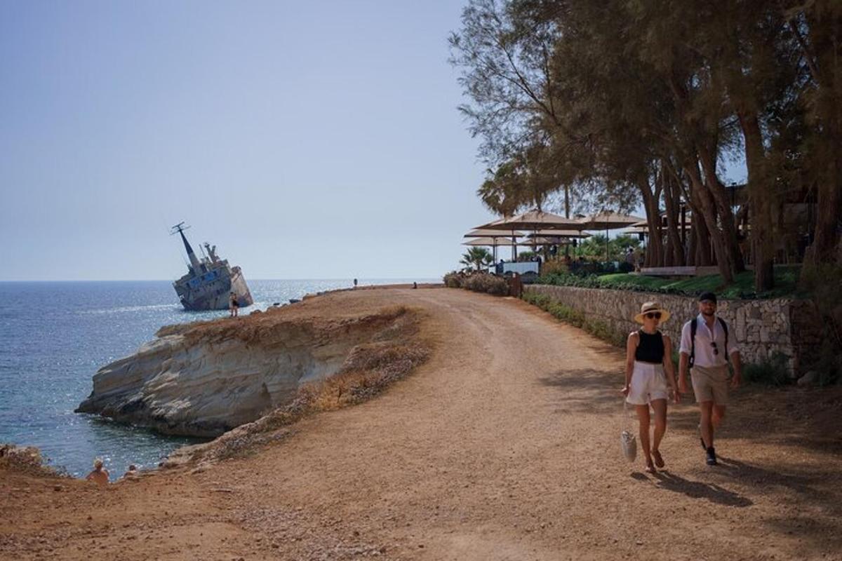 two people walking down a dirt road next to the ocean
