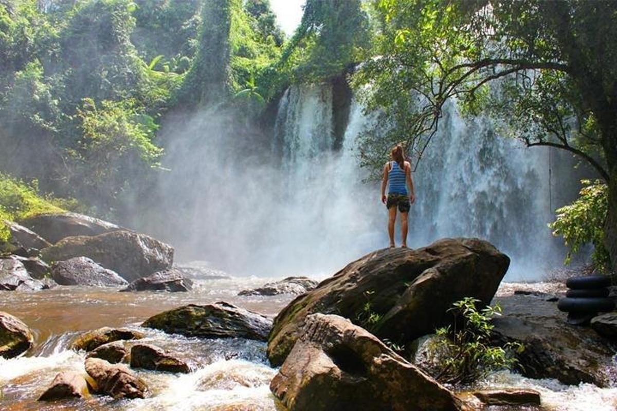 una persona in piedi su una roccia di fronte a una cascata
