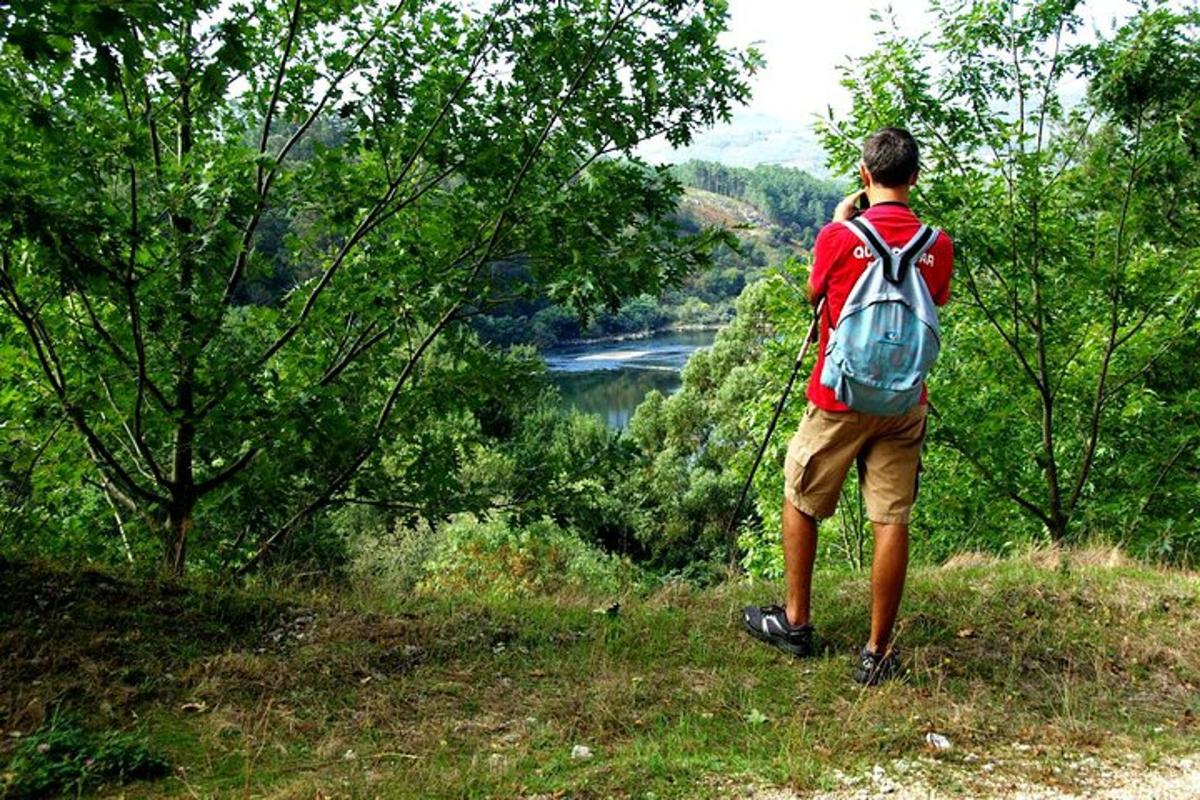 moški z nahrbtnikom stoji na hribu s pogledom na reko