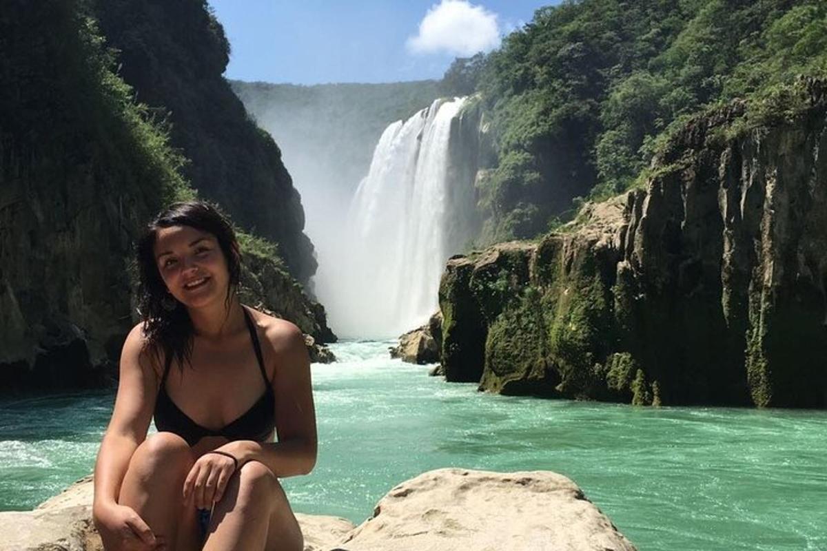 a woman sitting on a rock in front of a waterfall