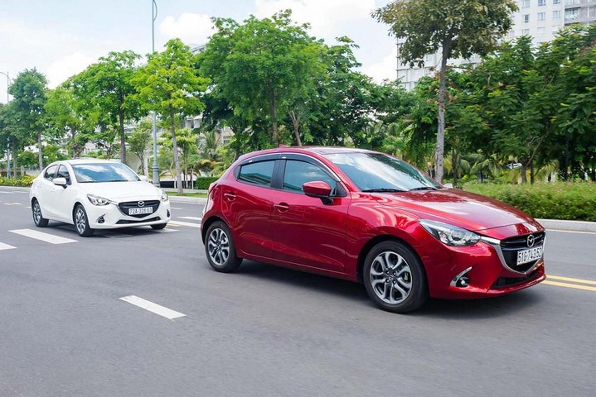 một chiếc xe màu đỏ đang chạy trên phố bên cạnh một chiếc xe màu trắng