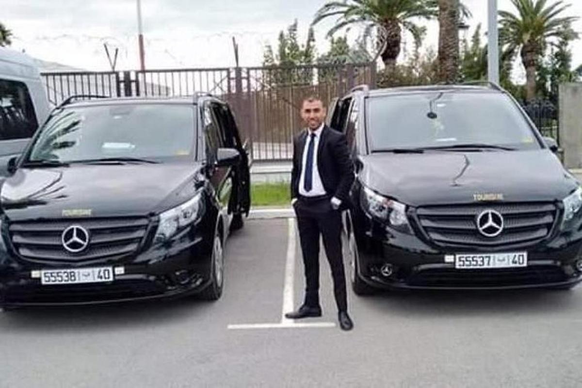 muž v obleku a kravatě stojící mezi dvěma auty