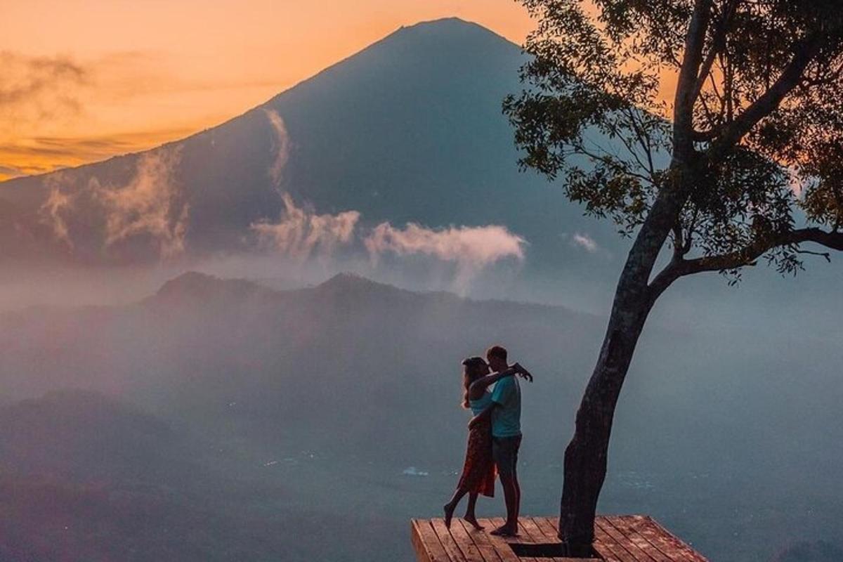 um casal em pé ao lado de uma árvore em frente a uma montanha