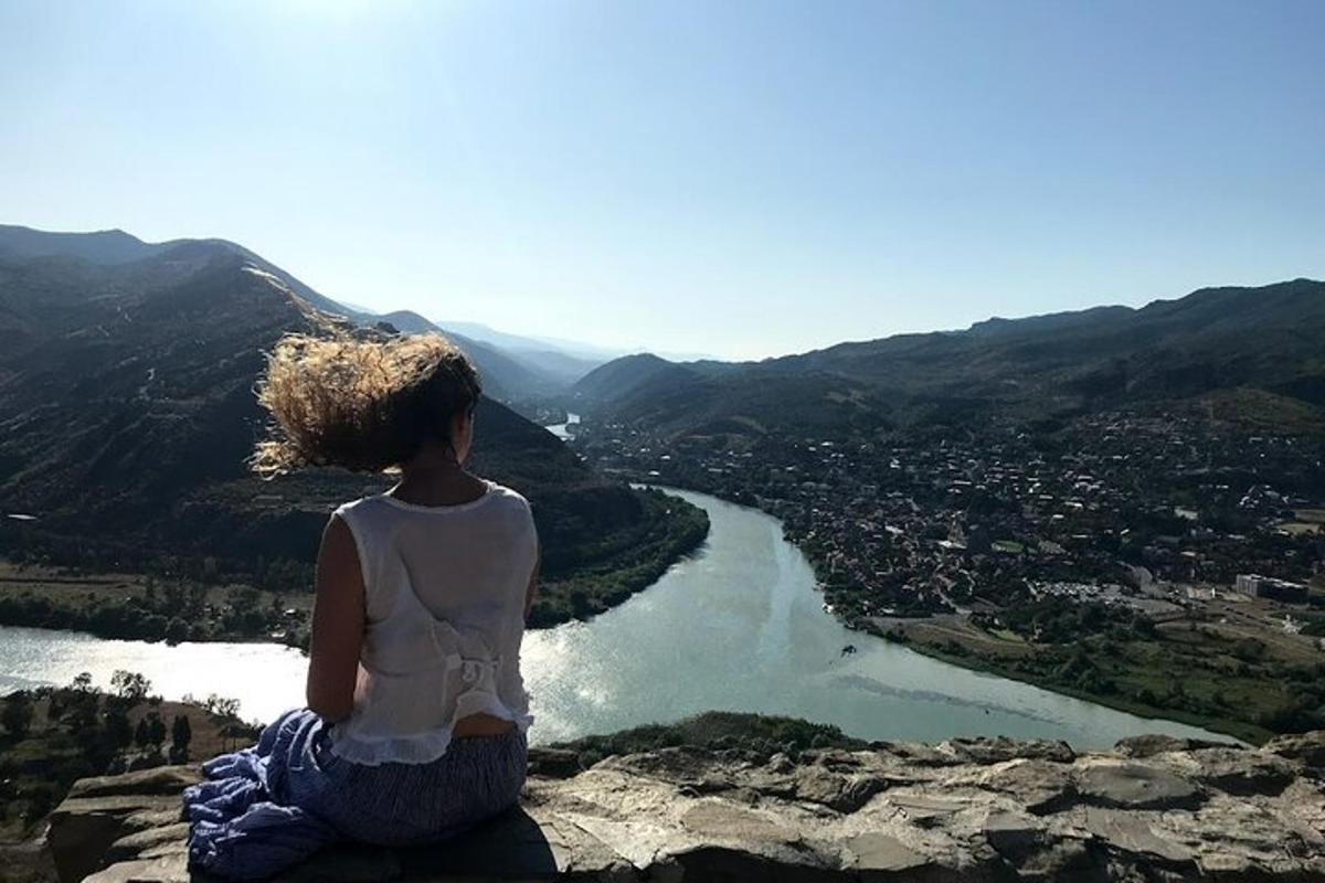 žena sedící na vrcholu skály s výhledem na řeku