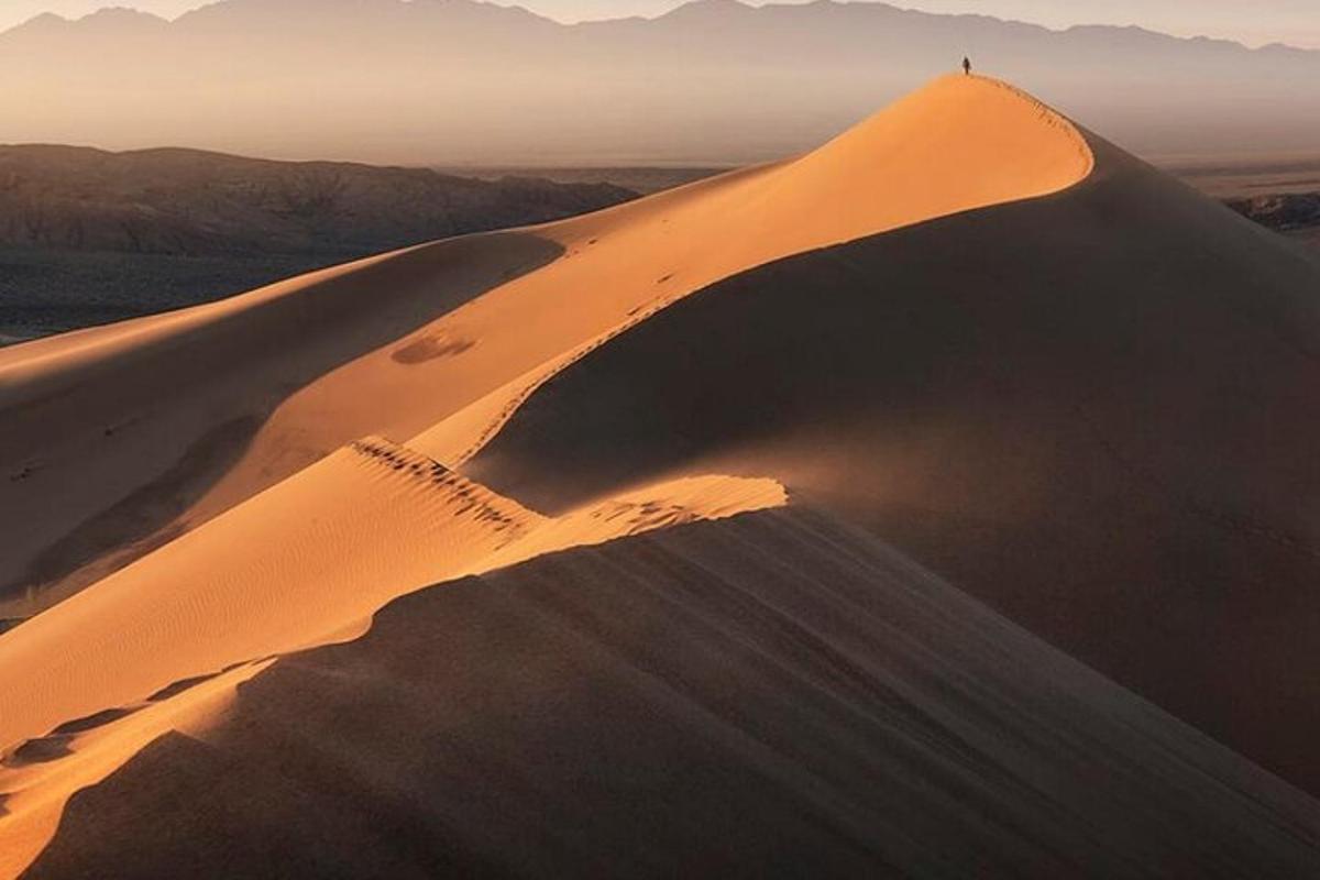 una persona parada en la cima de una duna de arena