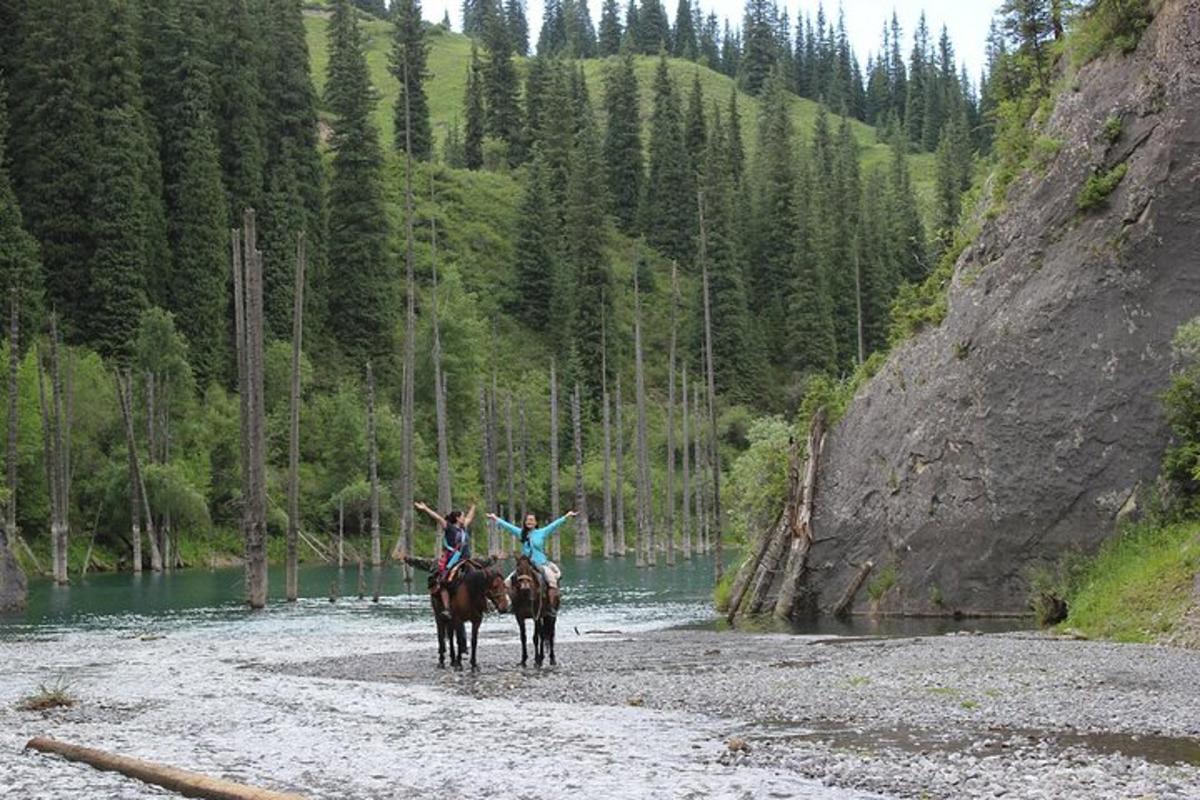 Dos personas montando a caballo en un río con los brazos en alto