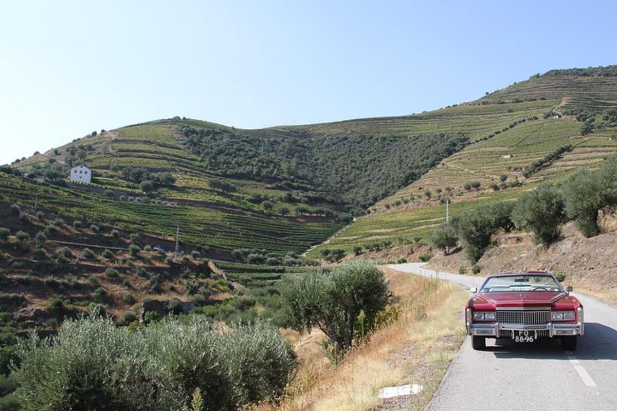a red car driving down a road next to a hill