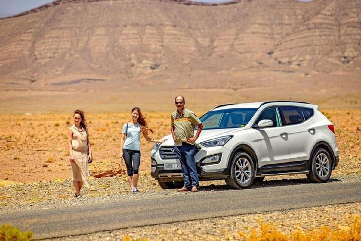 trys žmonės stovi šalia balto automobilio kelyje