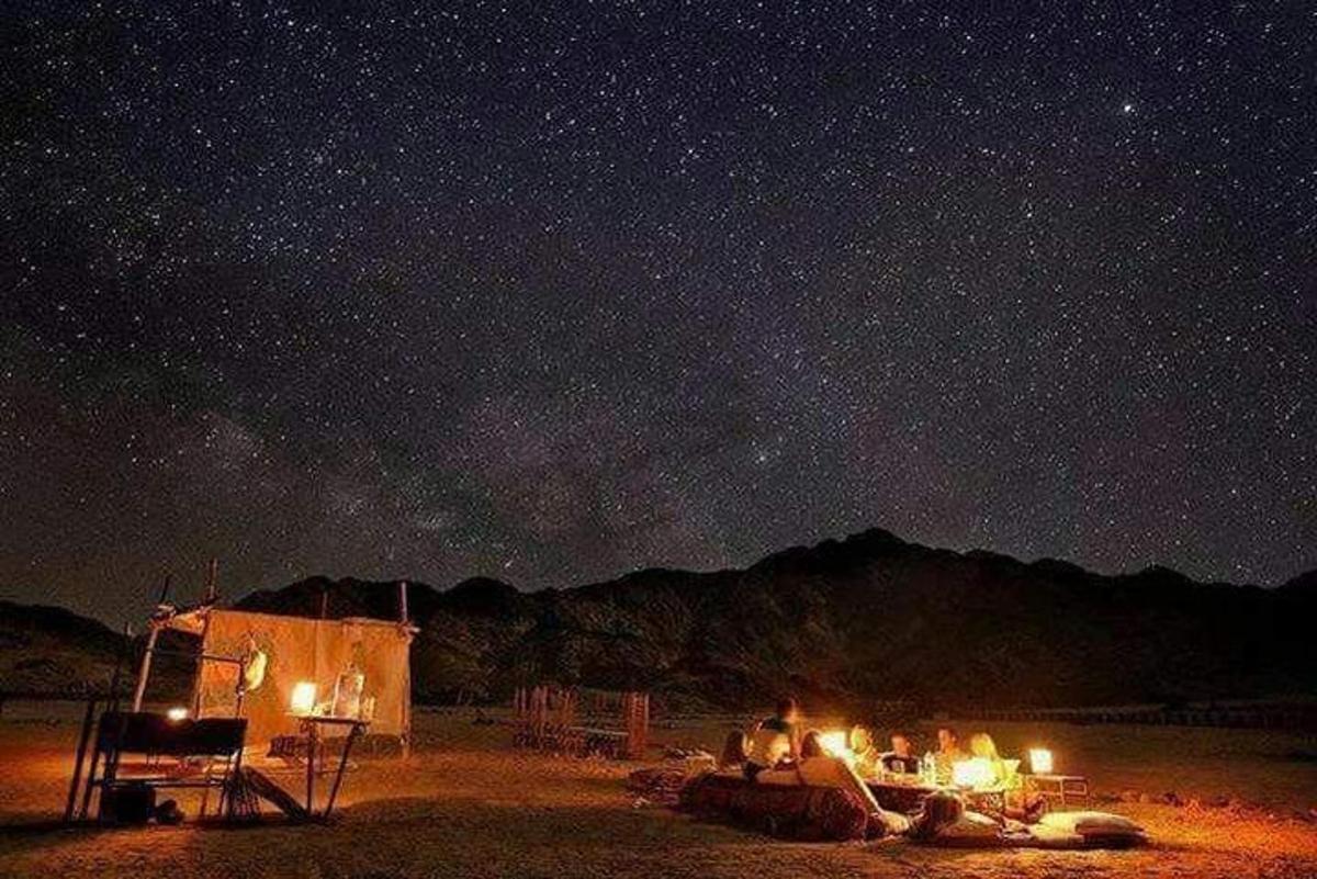 a group of people sitting around a tent under a night sky