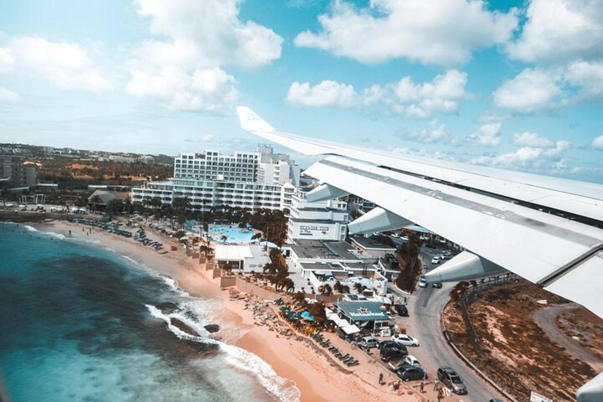 una ala d'avió volant sobre una platja amb un complex turístic